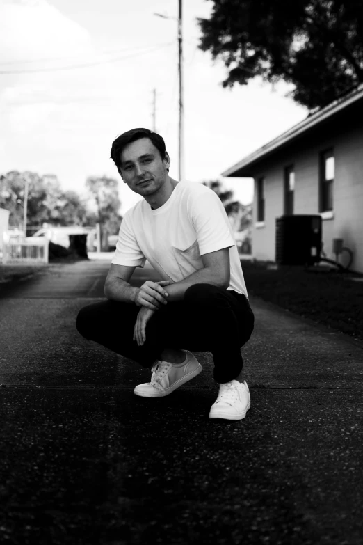 a man in white shirt sitting on street with sneakers