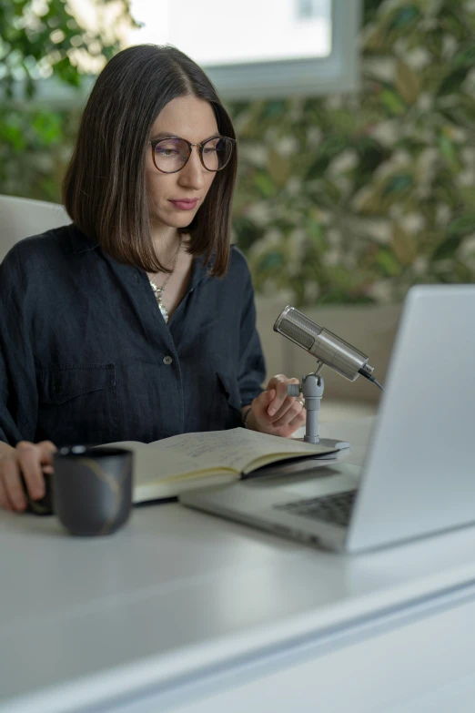 a woman in glasses sitting at her laptop writing