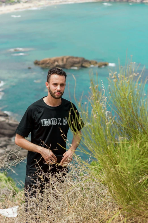 a man standing next to a grassy hill overlooking the ocean