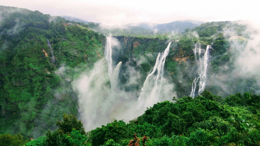 several tall waterfalls on a hill covered in clouds