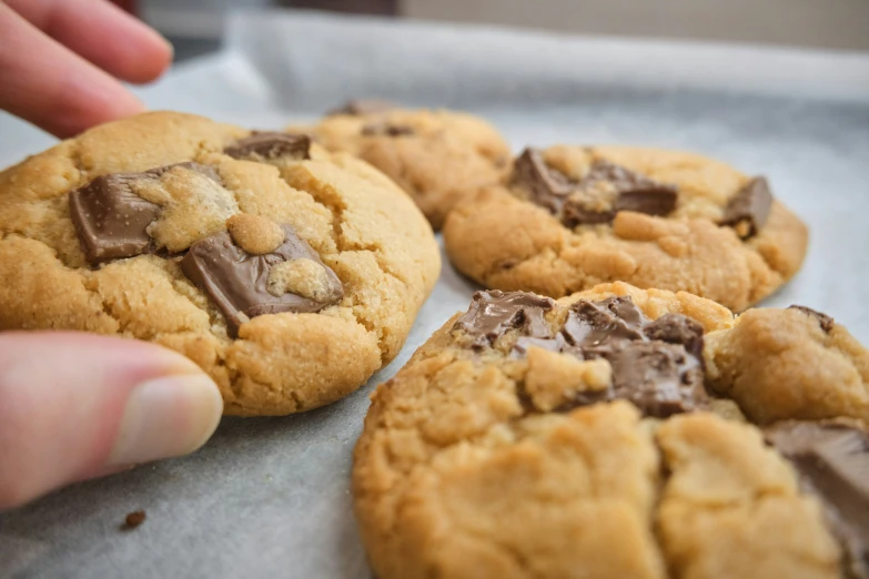 someone reaching for a chocolate chip cookie on a baking tray