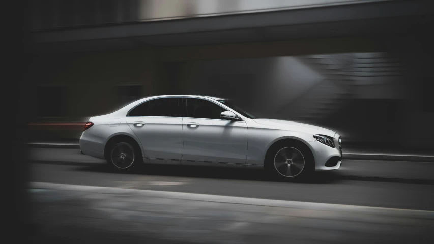 white mercedes e - class driving on road in urban setting