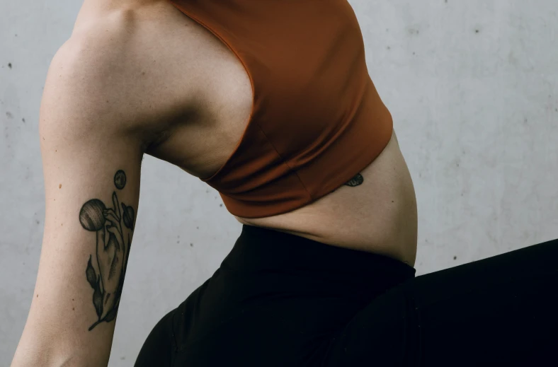 a woman with a back tattoo sits against a wall