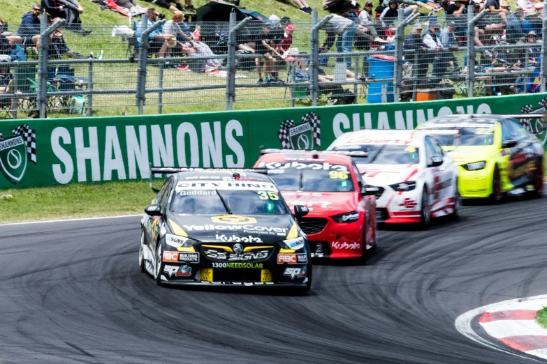 three cars going down a race track with their fans looking on