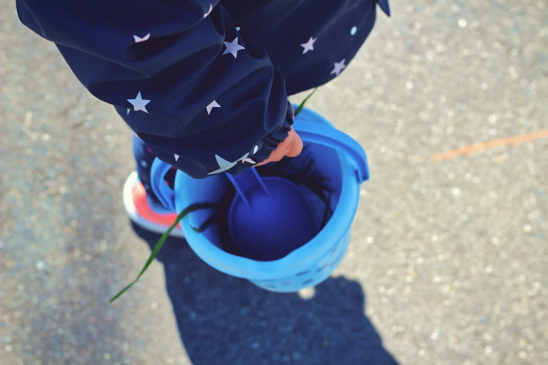 a child with an umbrella standing in a blue bucket