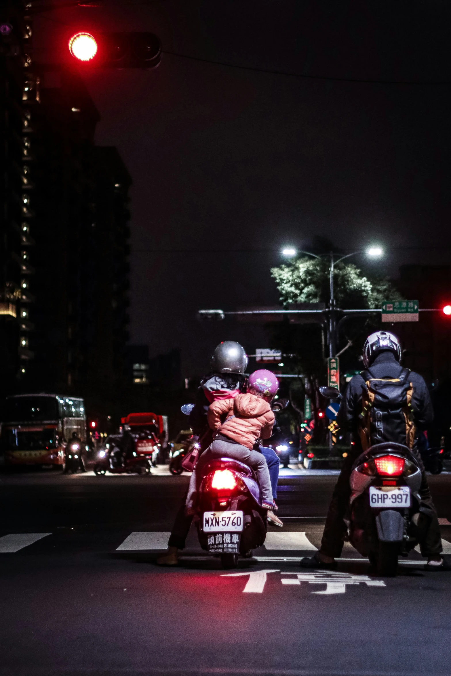 three people on motorcycles sit at a red light in the dark