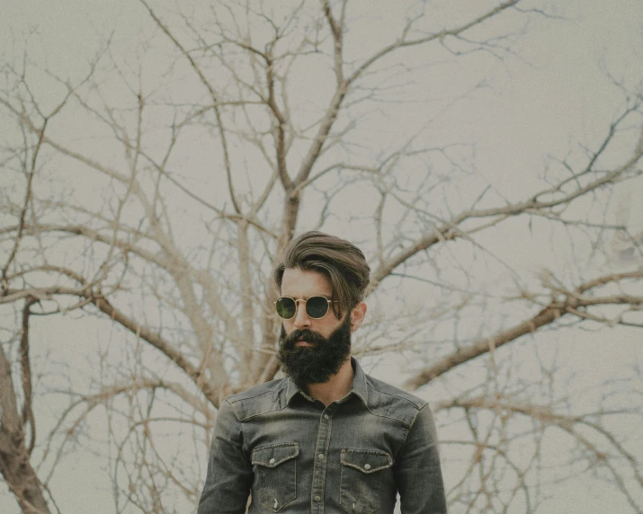 man with beard and glasses standing against trees