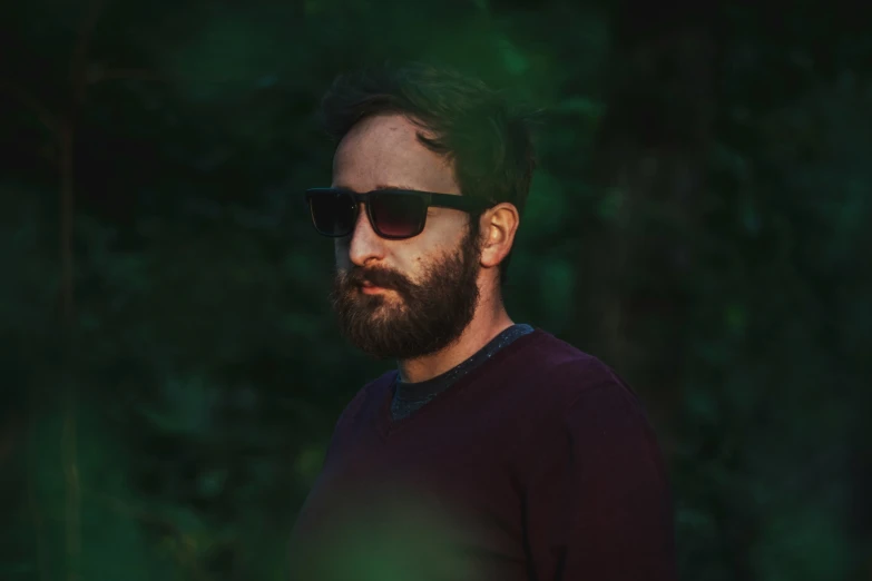 a man with a goatee and sunglasses in front of trees