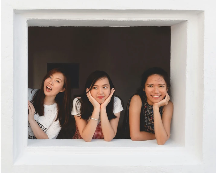 three girls pose behind a window to have their faces and hands together