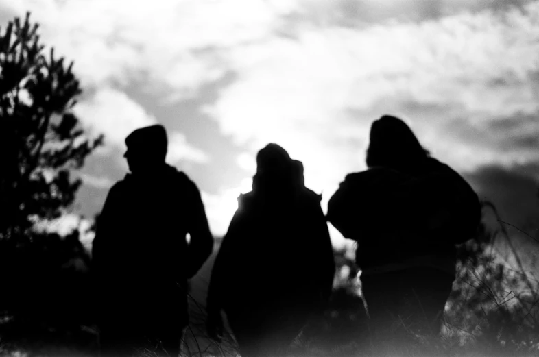 a silhouette of two people in a field with a cloudy sky behind them