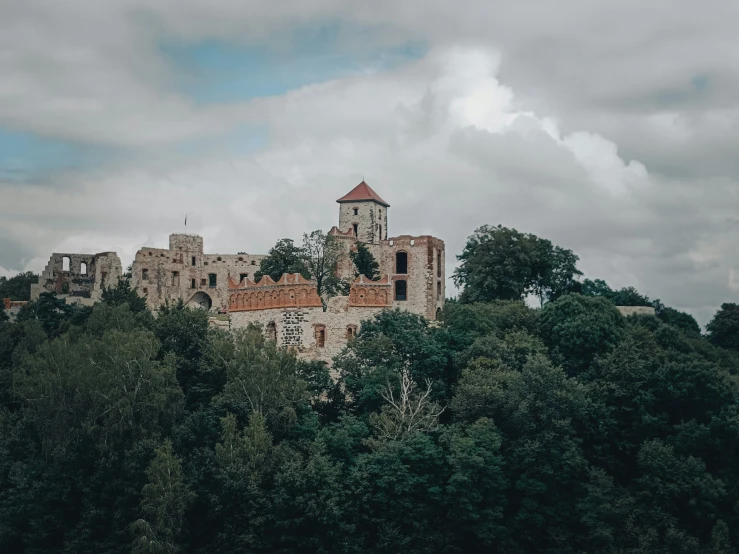 a tall castle sitting above trees under a cloudy sky