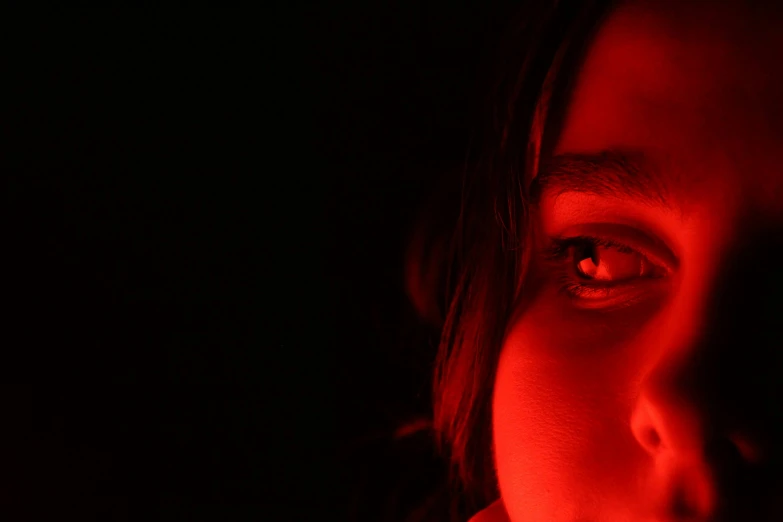 a dark room has an orange light on her left eye