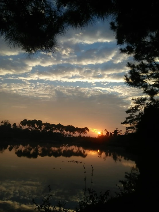 sun sets over the calm lake with fluffy clouds