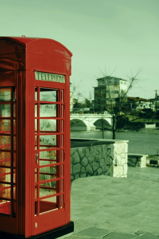 an old - fashioned red phone booth sits on a concrete sidewalk