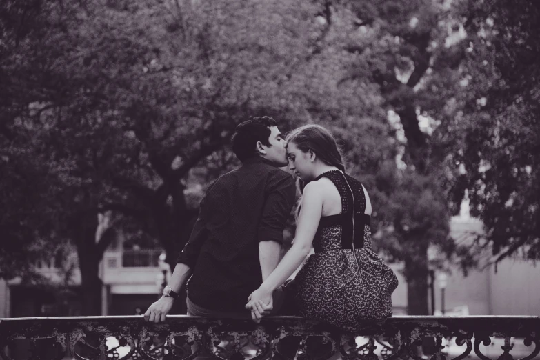 couple kissing on fence overlooking tree lined area