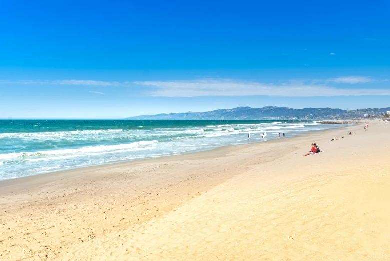 a beach filled with people and water next to a hill