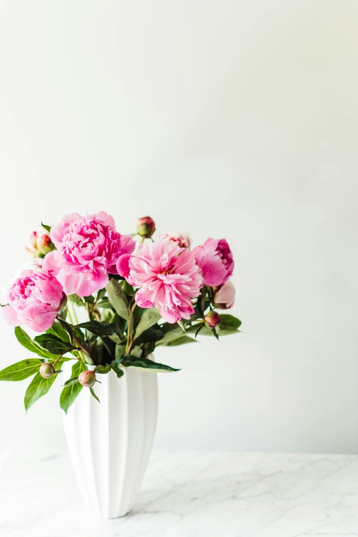 a white vase filled with pink flowers on top of a table