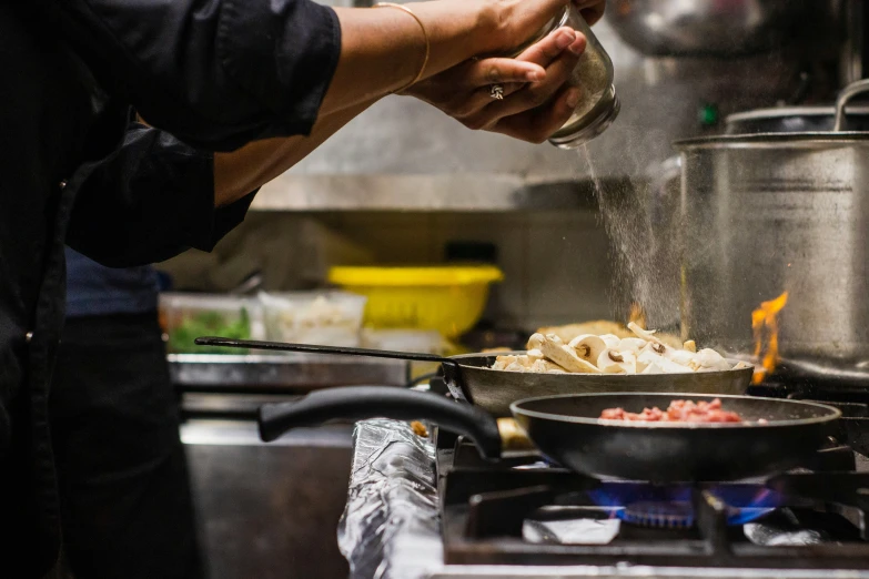 person pouring spices on food in a frying pan