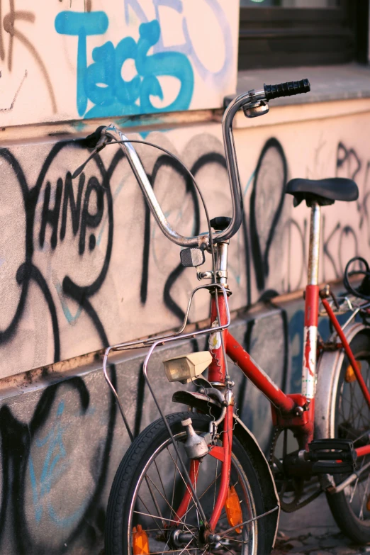a red bike parked against a wall with some graffiti on it