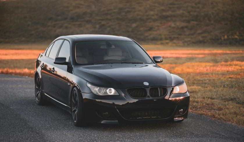 the black bmw car is parked in front of a field