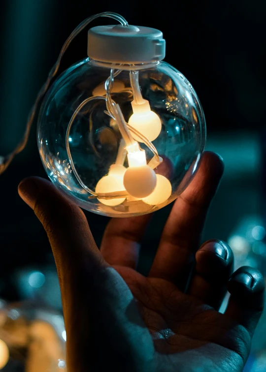 a person holds a floating glass jar with lights inside