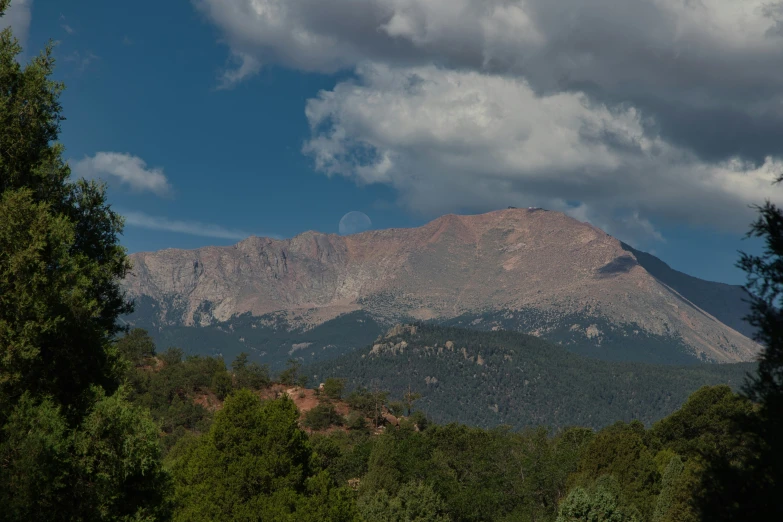 a lush green forest and large mountains under a partly cloudy sky