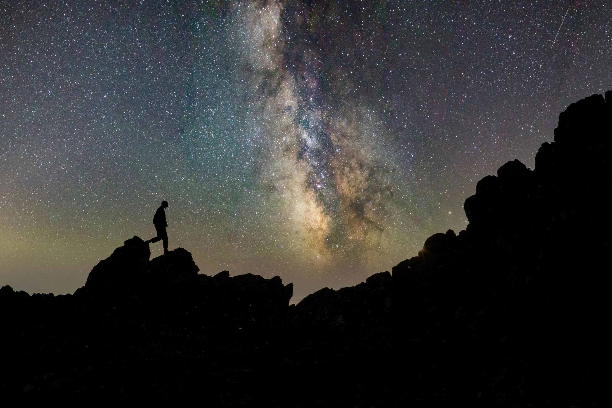 a person is standing on a cliff under a night sky filled with stars