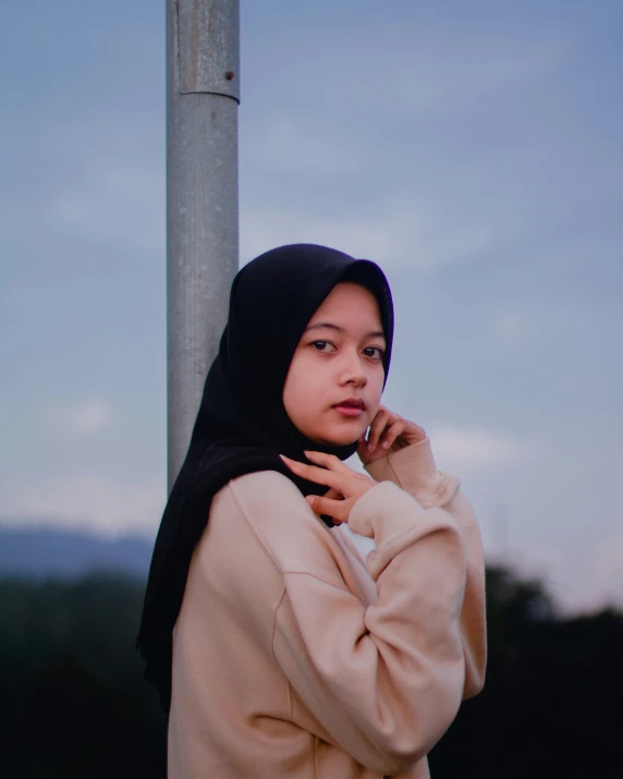 a woman wearing a hijab standing against a light post