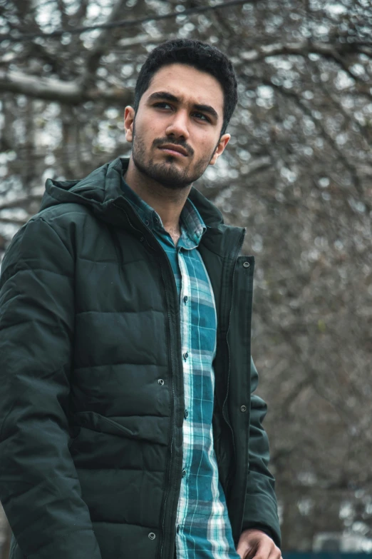 a man standing by a tree wearing a plaid shirt