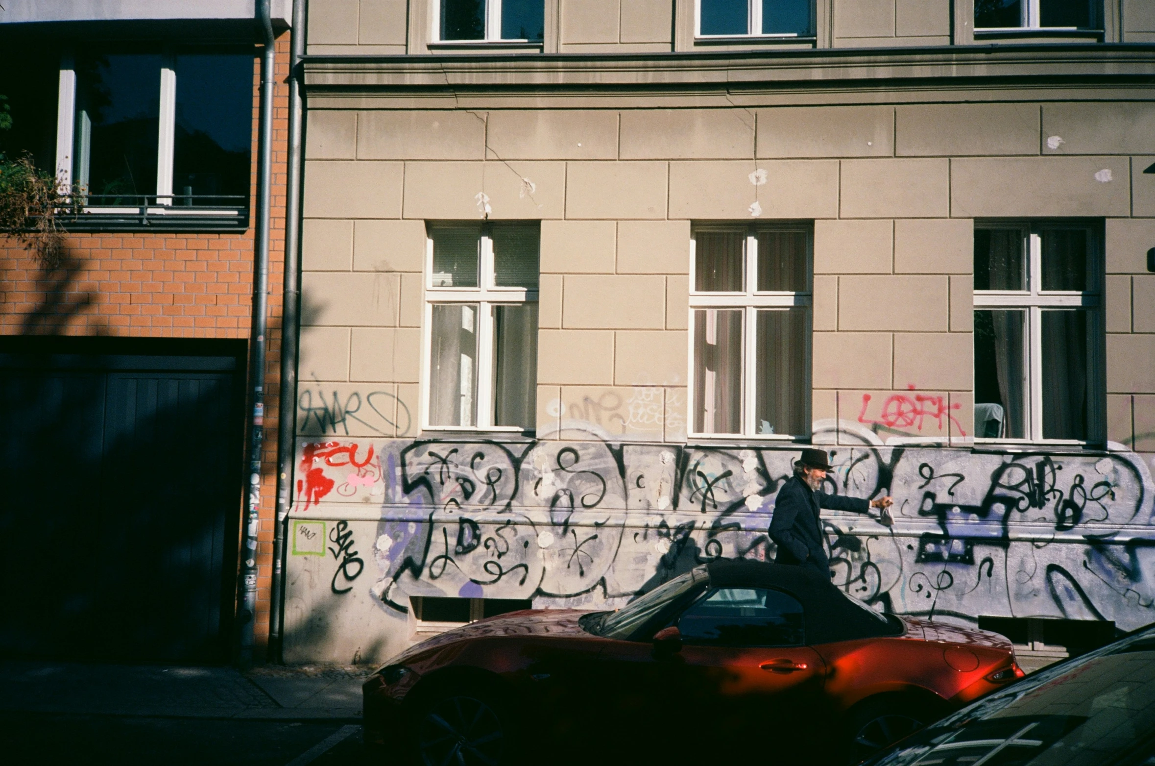 a red car parked on a street side by some graffiti