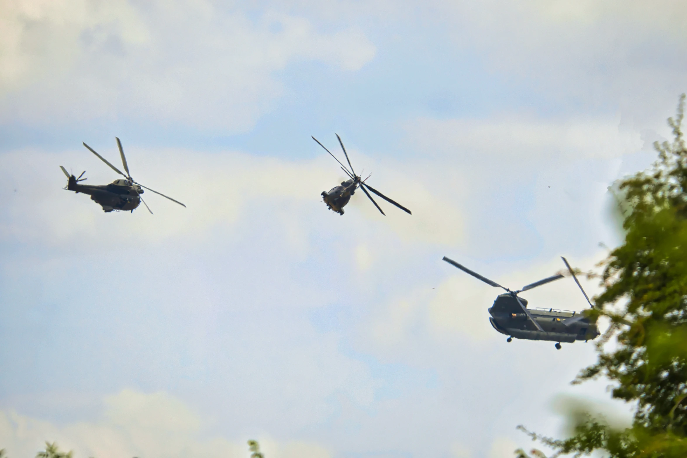 three military helicopters fly close together while another watches