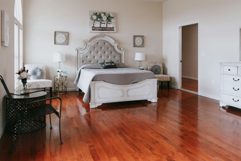 bedroom with wood floor and white bed, a chair, table and dresser