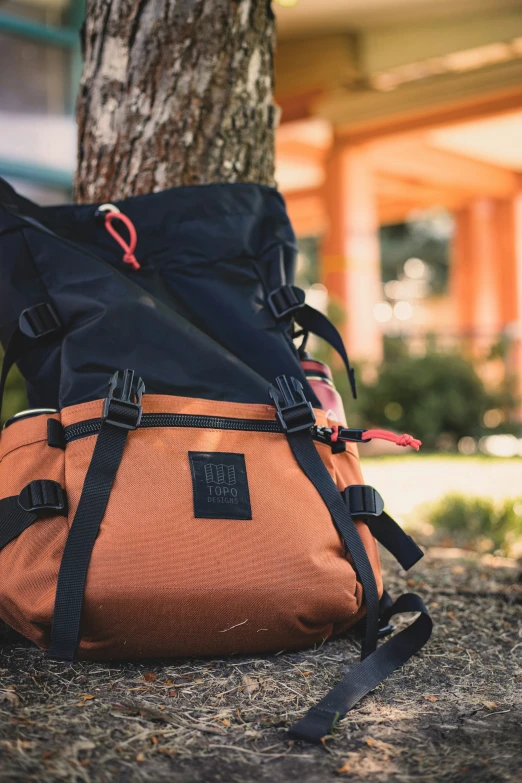 an orange and blue backpack laying under a tree