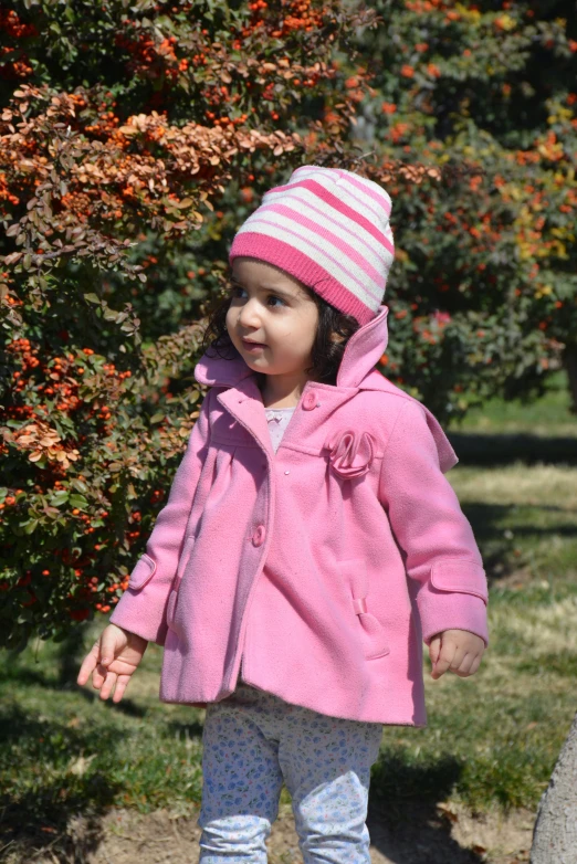 a little girl in pink coat walking on a sidewalk