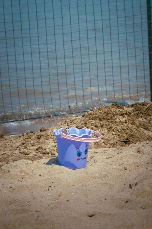 there is a blue and pink toy bucket on the beach