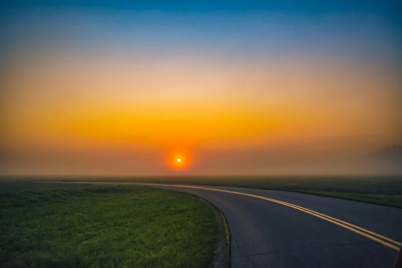 the sun is setting over a rural road