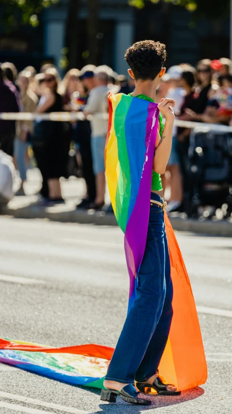 a  standing in the street holding a rainbow colored kite