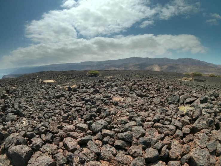 several black rocks and some hills under a cloudy sky