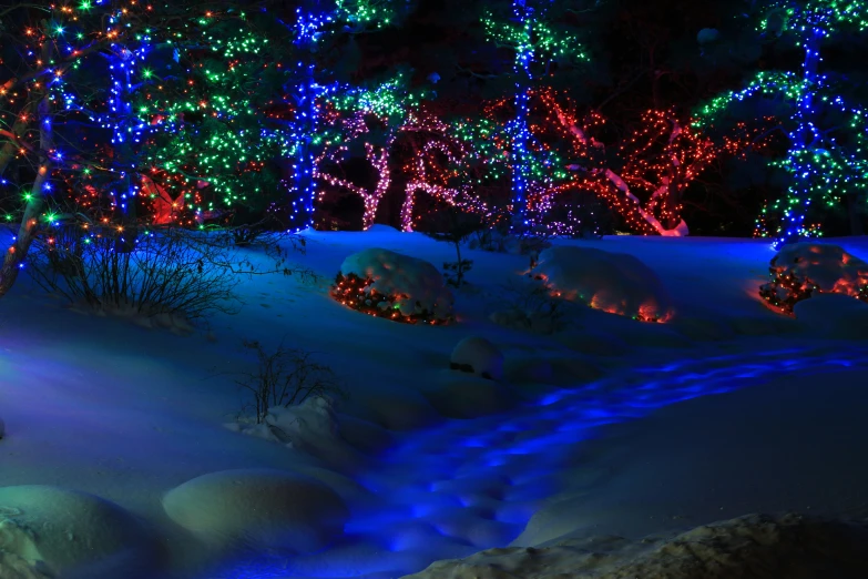 a very colorful christmas scene with lights, stream, and trees