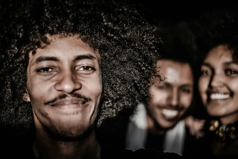 two smiling people with afros in a dark area