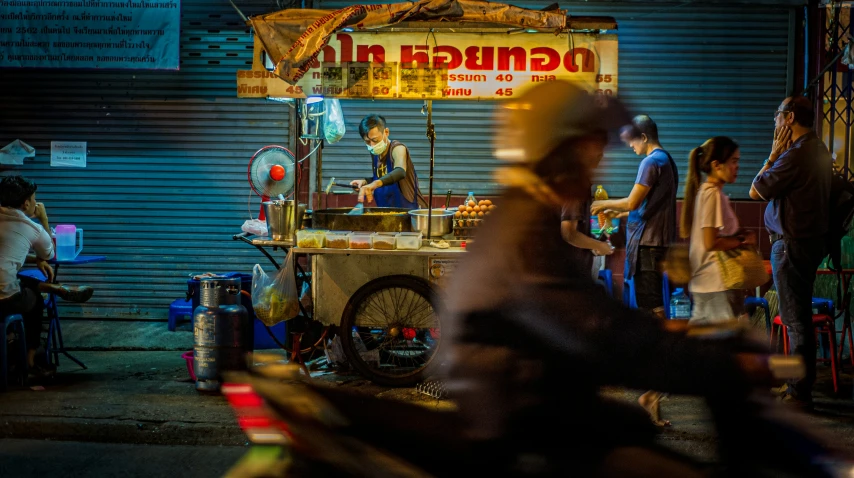 a man riding his bike down the street next to a food stand