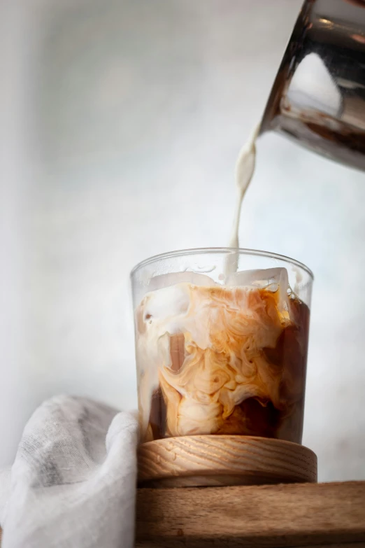 a person pouring some milk into an ice tea cup