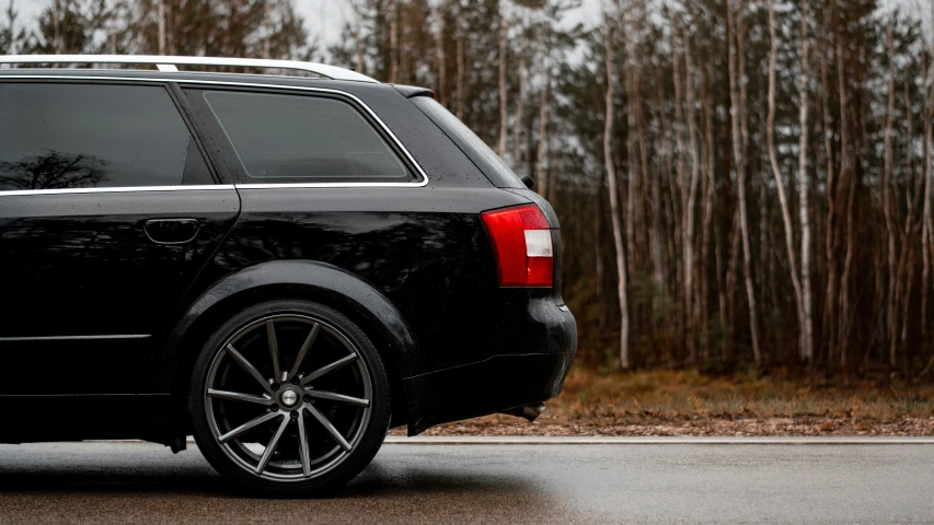 the back of a black minivan parked near the woods