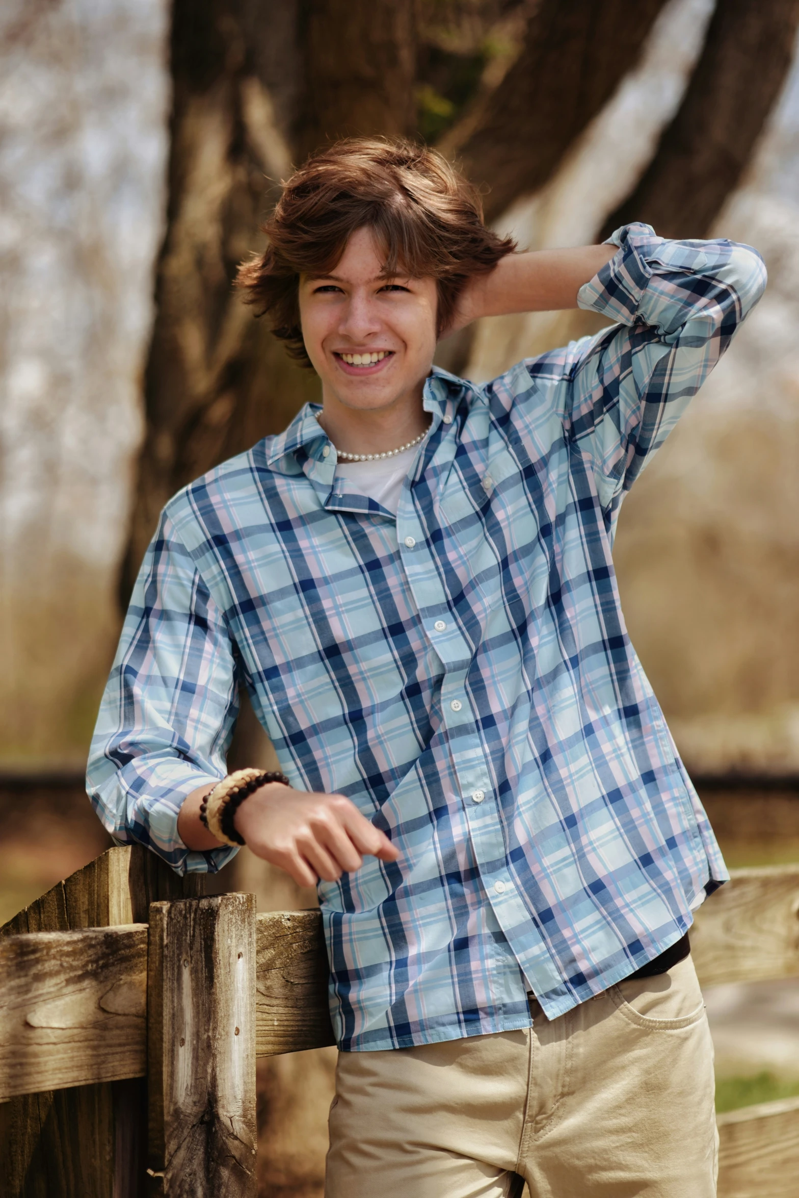 a young man smiling by a fence holding his hand on his head