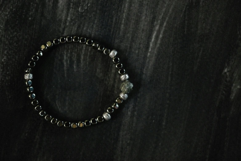 a bead celet with a diamond charm is sitting on a dark surface