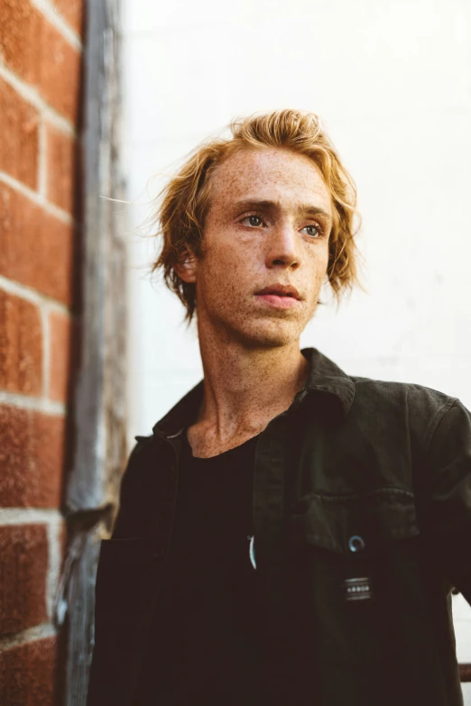 a man standing next to a brick wall and leaning on a brick wall