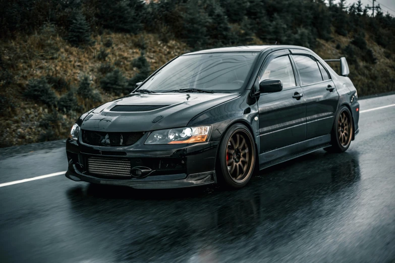 a black car that is driving down a rain soaked road