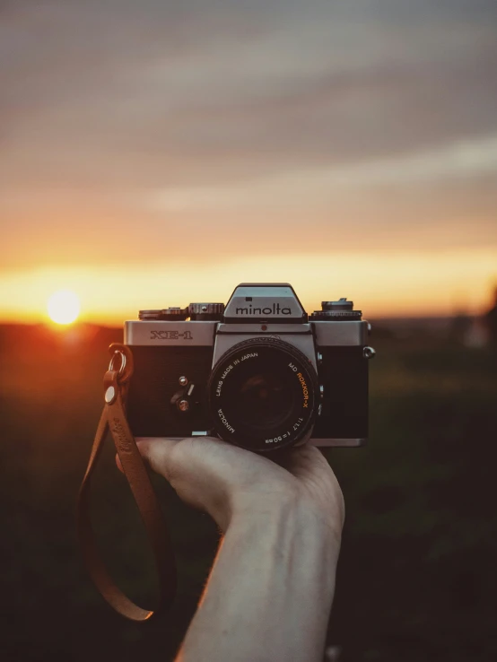 a person holding up a small camera with a sunset in the background
