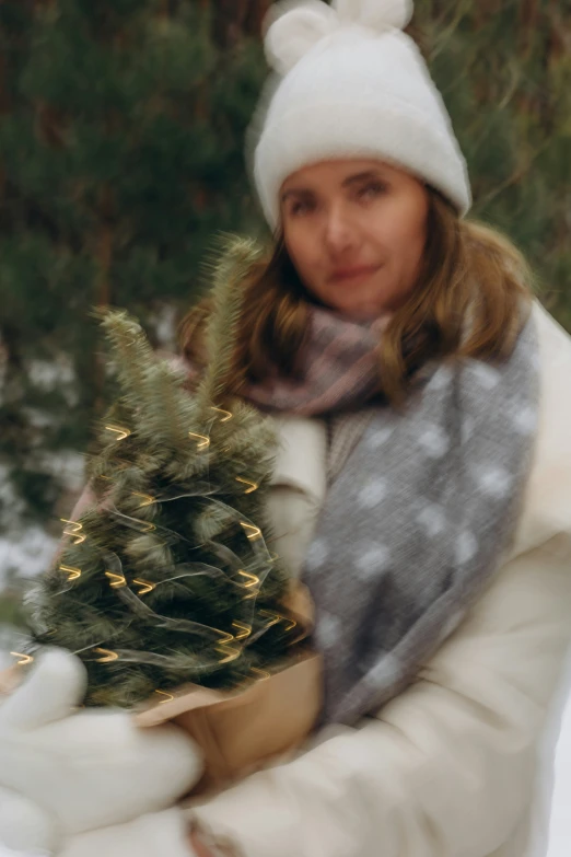 a woman in white jacket holding up a small christmas tree