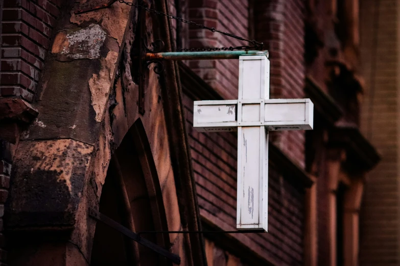 an old, weathered cross hanging from the side of a brick building